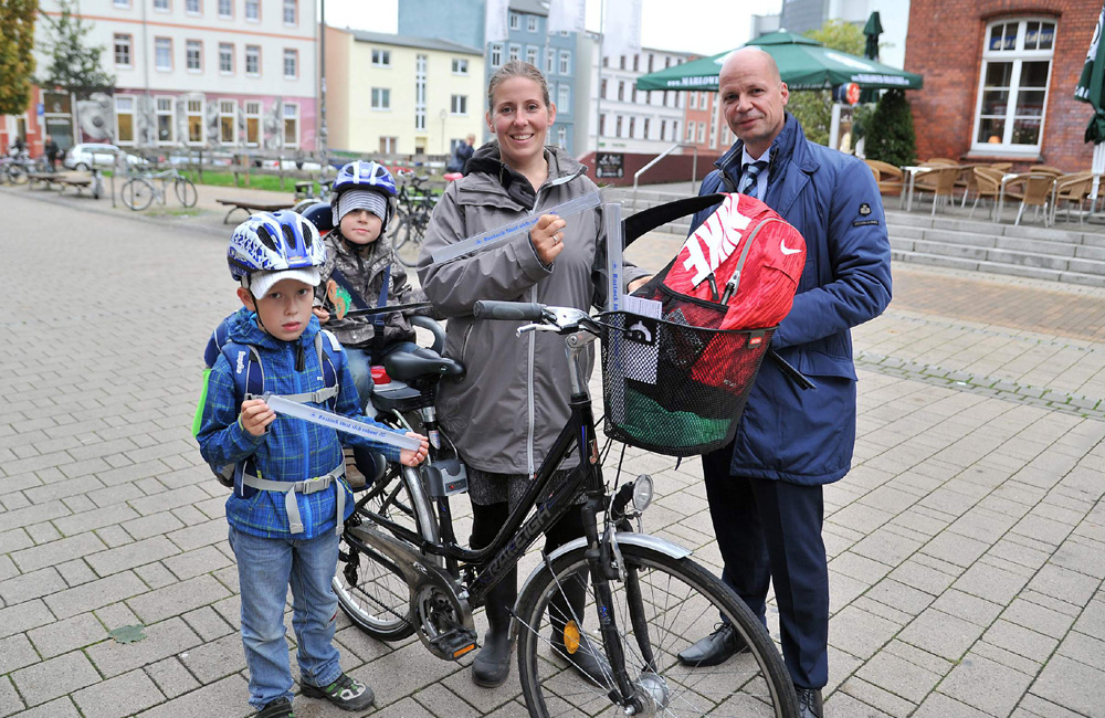 Senator Dr. Chris Müller übergab Stefanie Labitzke und ihren Kindern Max und Hannes Leuchtbänder mit der Aufschrift „Rostock lässt sich sehen“. Foto: Joachim Kloock